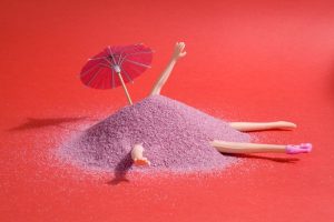 Photo Of A Doll Buried In Purple Sand With An Umbrella.