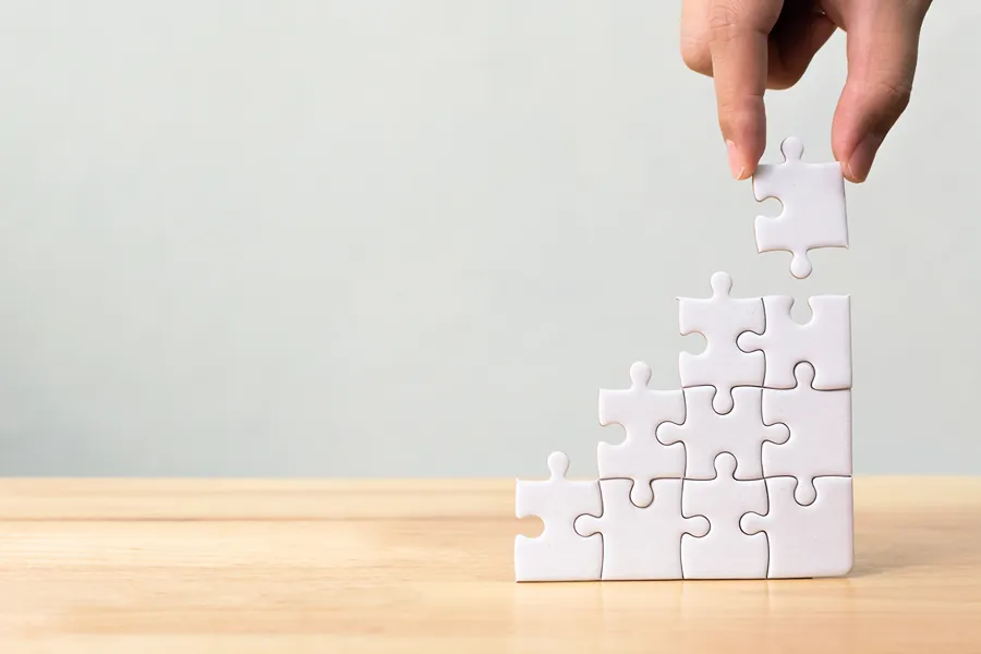 A Hand Putting A Puzzle Piece On Top Of A Stepped Puzzle.
