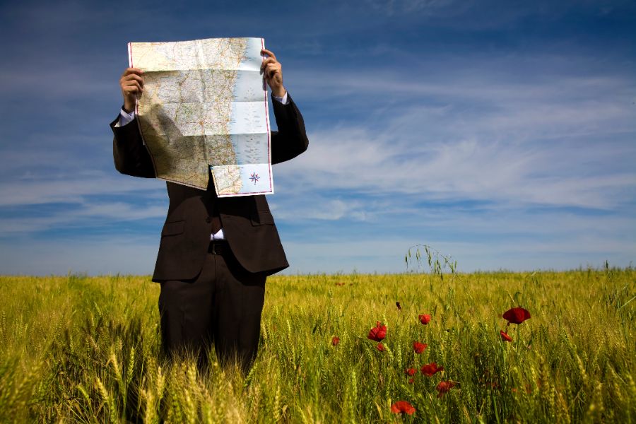 A Business Person Lost In A Field Trying To Read A Map The Wrong Way.