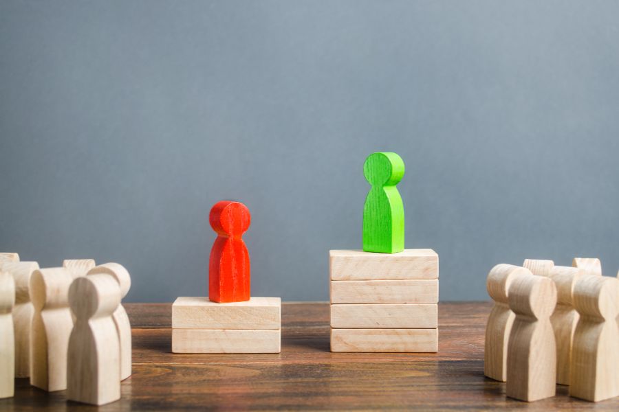 Wooden Blocks Are On Two Podiums, One Is Taller Than The Other, And There Is An Audience Of Wooden Blocks Around Them.